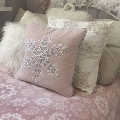 a bed topped with lots of pillows covered in snowflakes and furry throw pillows