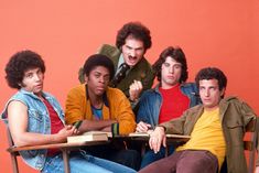 four young men sitting at a table with an open book in front of their faces