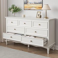 a white dresser with two drawers and a painting on the wall above it in a living room