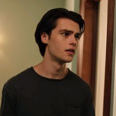 a young man standing in front of a mirror wearing a black t - shirt and looking at the camera