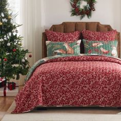 a bed with red and green comforter next to a christmas tree