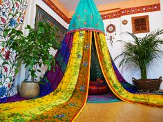 a canopy bed covered in colorful fabric next to a potted plant on the floor