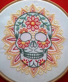 a white embroidered skull with red flowers on it's forehead and eyes, sitting in front of a red background