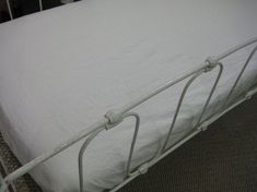 a metal bed frame with white sheets and pillows on top of carpeted flooring