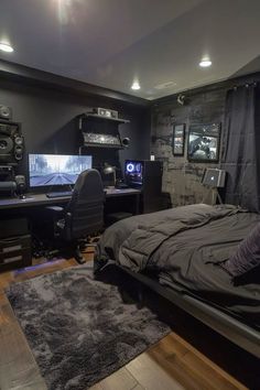 a bedroom with a bed, desk and two monitors on the wall in front of it