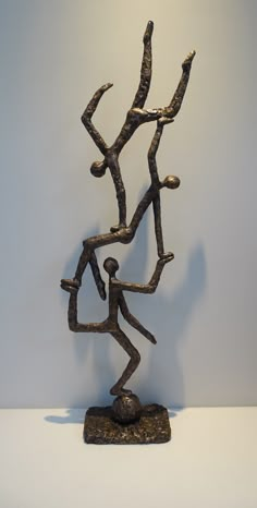 a bronze statue of a person holding two branches on top of a rock in front of a white wall