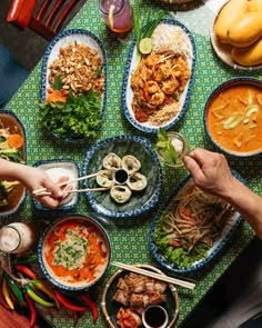 people are sitting at a table with many bowls of food on it and chopsticks in their hands