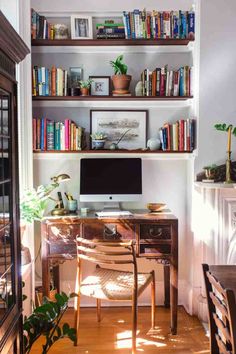 a desk with a computer on top of it next to a book shelf filled with books