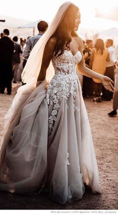 a woman in a wedding dress and veil walking down the street with people behind her