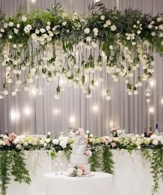 a white wedding cake sitting on top of a table covered in flowers and greenery