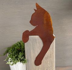 a metal cat sitting on top of a wooden block next to a potted plant