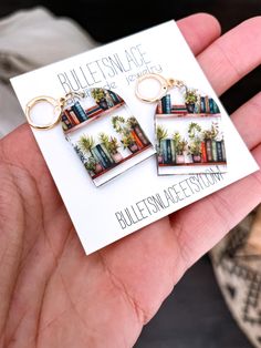 a pair of bookshelf shaped keychains are being held in front of a card