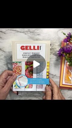 a person holding up a book on top of a marble table next to flowers and cards