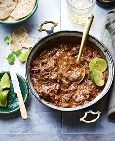 a pot full of chili with tortillas and limes next to it on a table