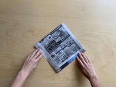 two hands reaching for a newspaper on a wooden table