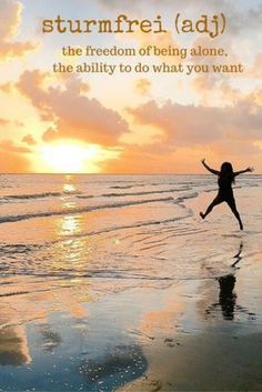 a woman jumping in the air on top of a beach next to the ocean at sunset