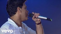 a man singing into a microphone with his hands in the air while wearing a white shirt