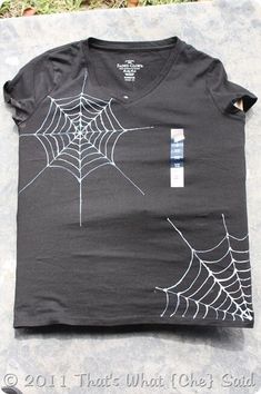 a t - shirt with spider webs on it is laying on the ground in front of some grass