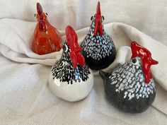 three ceramic roosters sitting on top of a white cloth next to eachother