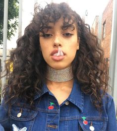 a woman with long curly hair wearing a collar and piercings on her nose is making a funny face