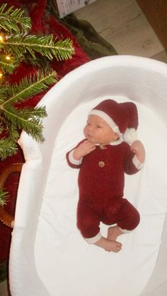 a baby wearing a santa hat is in a crib next to a christmas tree