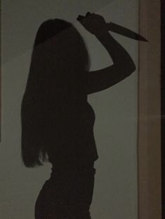 the shadow of a woman holding a knife in front of her face and standing next to a window