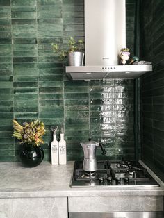 a stove top oven sitting inside of a kitchen next to a wall covered in green tiles