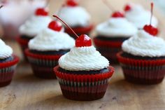 cupcakes with white frosting and cherries on top are sitting on a table