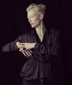 a woman with blonde hair standing in front of a black background wearing a black shirt