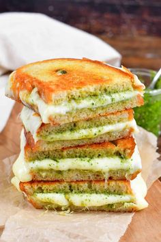 a stack of four grilled sandwiches sitting on top of a wooden cutting board next to a cup of pesto