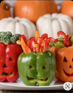 three peppers with faces carved into them on a plate next to pumpkins and broccoli