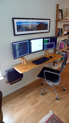 a computer desk with two monitors and a laptop on it in front of a bookshelf