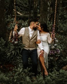 a bride and groom sitting on a swing in the woods