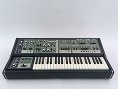 an electronic keyboard sitting on top of a white table next to a black case with buttons and knobs