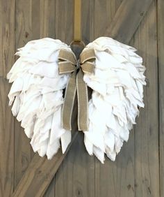 a white angel wings hanging on the side of a barn door with a ribbon tied around it