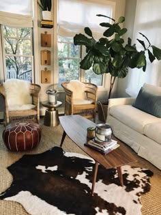 a living room filled with lots of furniture and plants on top of the tables in front of large windows