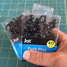 a person holding some black plastic push pins in their hand on a green table top