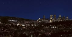 the hollywood sign is lit up at night in front of a cityscape with skyscrapers