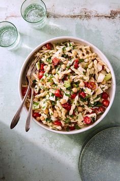 a bowl filled with pasta salad next to two empty glasses on a counter top,