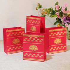 four red bags with gold designs on them sitting on a table next to some flowers