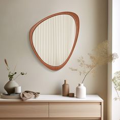 an oval mirror on the wall above a dresser with vases and other decor items