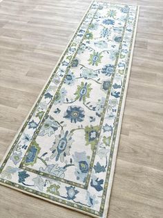 a white rug with blue and green flowers on the floor next to a wooden floor