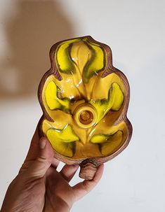 a hand is holding a yellow and green glass vase in the shape of a flower