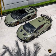 two green sports cars parked next to each other on a cement surface with palm trees in the background