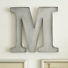 the letter m is made out of metal and sits in front of two framed pictures