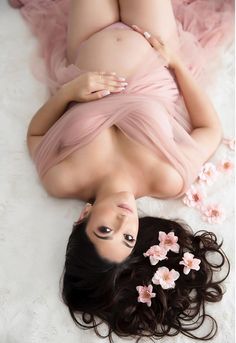 a woman laying on top of a bed with flowers in her hair and wearing a pink dress