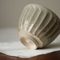 a white vase sitting on top of a wooden table next to a piece of paper