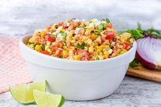 a white bowl filled with corn salad next to a cutting board and lime wedges