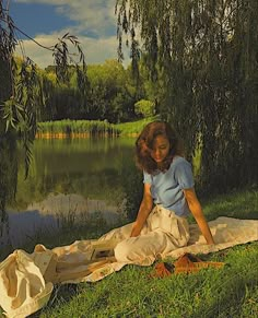 a painting of a woman sitting on a blanket by the water