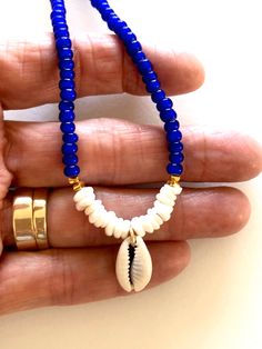 Beaded shell choker with cobalt blue African glass beads, Hawaiian white puka shells, genuine cowrie shell and Karen Hill Tribe 24k gold vermeil accents. Beaded summery necklace features vintage cobalt blue African white heart trade beads and genuine sea shells. Little white Hawaiian puka shells and genuine cowrie shell focal. Karen Hill Tribe 24k gold vermeil cube beads add fabulous accents. Beaded necklace closes with 14k gold fill spring ring clasp and findings. Blue Strand Shell Necklace For Vacation, Blue Shell Strand For Beach, Blue Shell Beaded Bracelets For Beach, Blue Shell-shaped Shell Necklace For Vacation, Blue Shell-shaped Necklace For Beach, Blue Shell-shaped Necklace For Vacation, Blue Shell-shaped Adjustable Necklace, Blue Shell Necklace For Beach, Blue Shell Beaded Bracelet As Gift